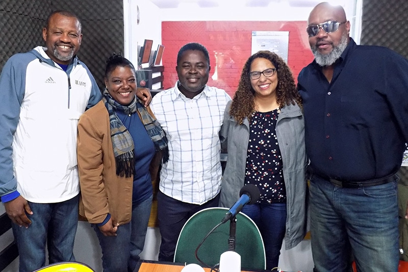 Rose aparece de casaco, roupa social e cabelos presos, sorrindo. Juntos a ela estão três outros comunicadores e convidados homens, todos negros. Um a sua esquerda, outro depois dela no meio, e um terceiro no fim da foto. Entre este segundo e último há uma mulher, também negra, mas de cabelo encaracolado e menos retinta. Todos usam roupas sociais e sorriem em um local, cujo fundo é o estúdio ou uma sala de espera de uma rádio.